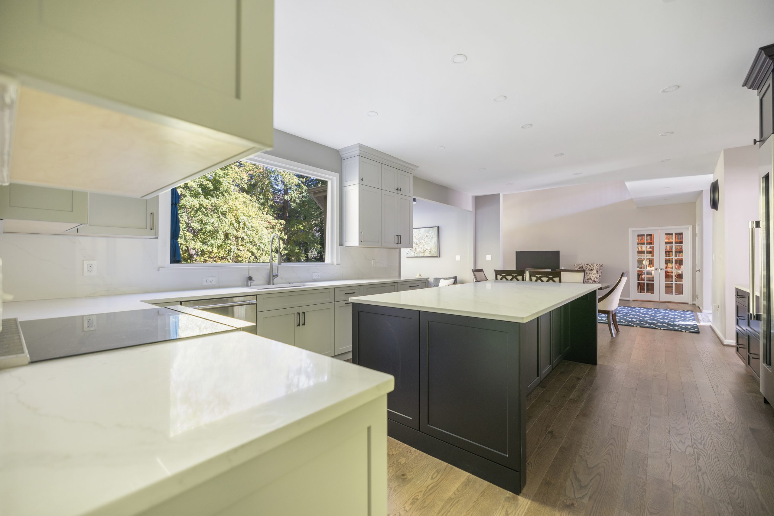 Dark green kitchen island with white quartz top in a Northern Virginia kitchen with wide aisles, opening to a dining room