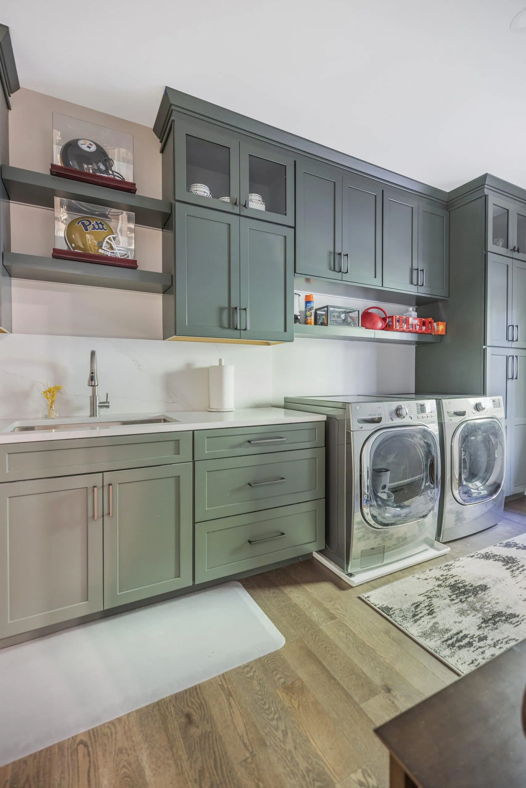 Laundry room with sage green cabinets, a sink, a folding counter and a front loading washer and dryer