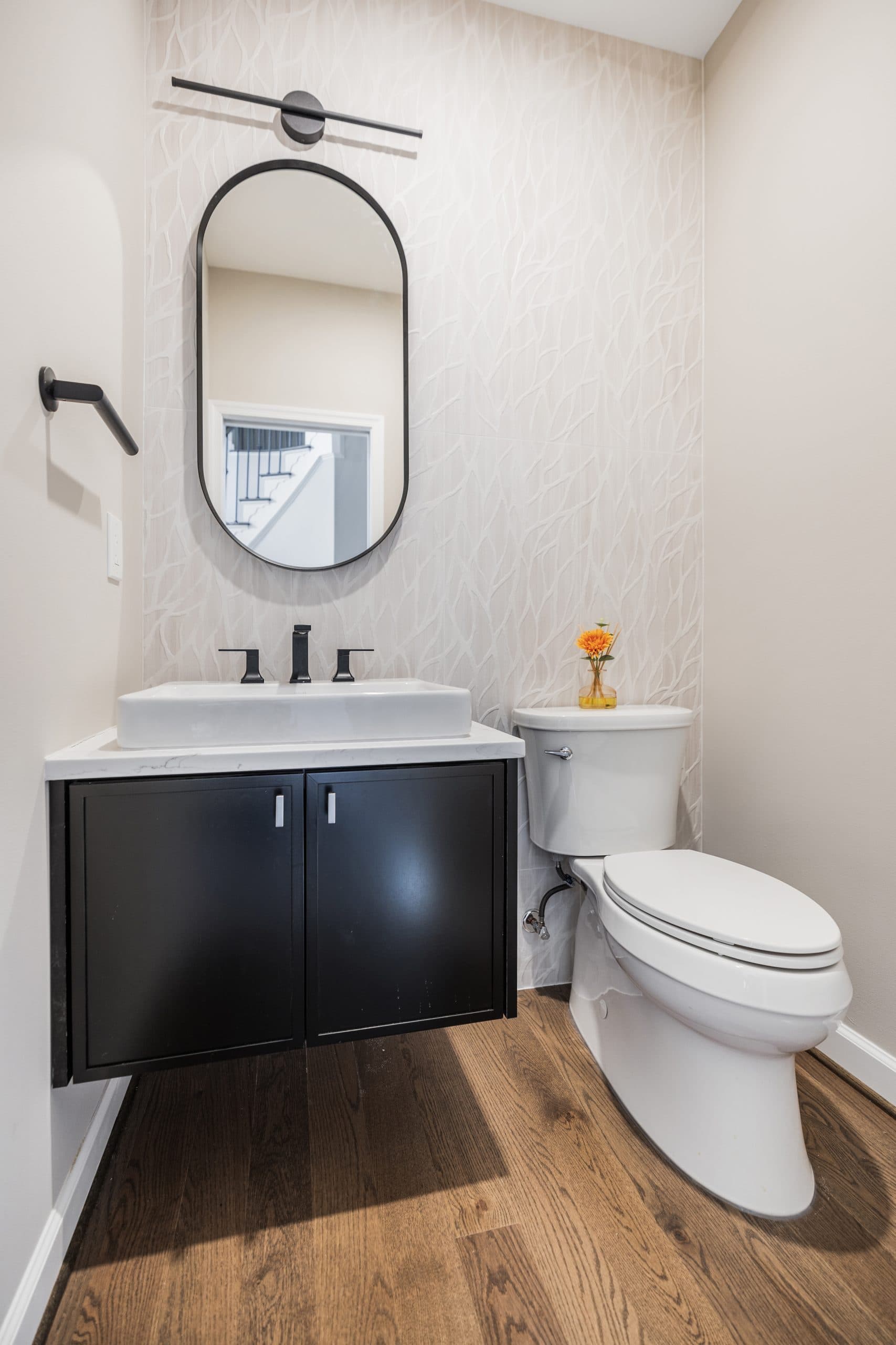 Powder room in a Northern Virginia home with a wall hung black vanity with knee clearance, lever faucet, oval mirror and comfort height toilet