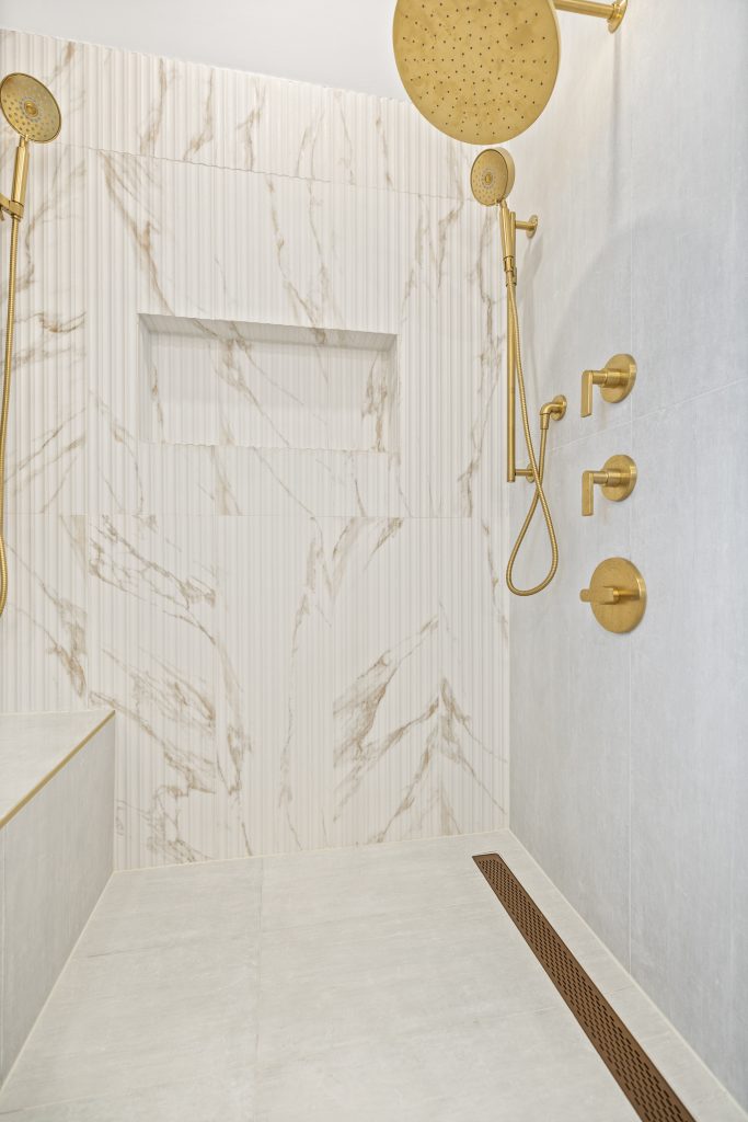 After: inside the shower, fluted marble look wall, recessed niche, gold rain head and hand shower