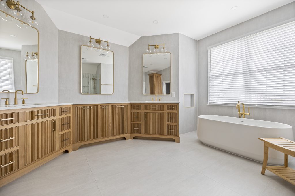 After: L-shaped double vanity with three gold framed mirrors and sconces, freestanding tub under the window