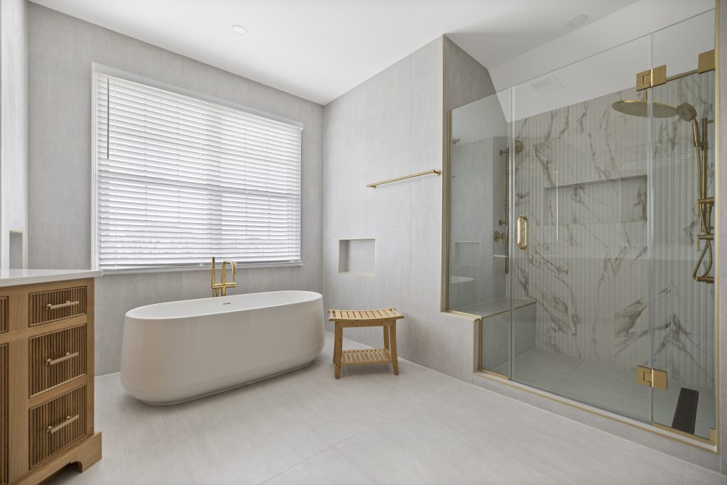 After: freestanding tub under the window beside the new shower with a marble look feature wall and bench