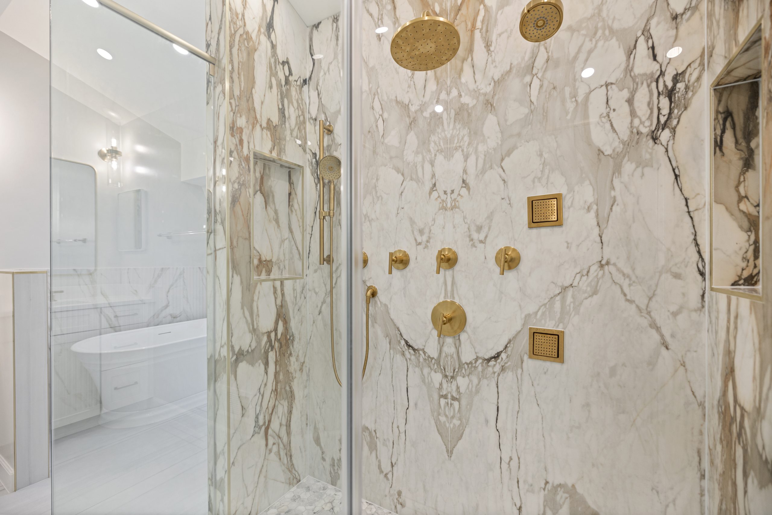 Luxury shower with gold fixtures and marble walls showing premium bathroom remodel finishes