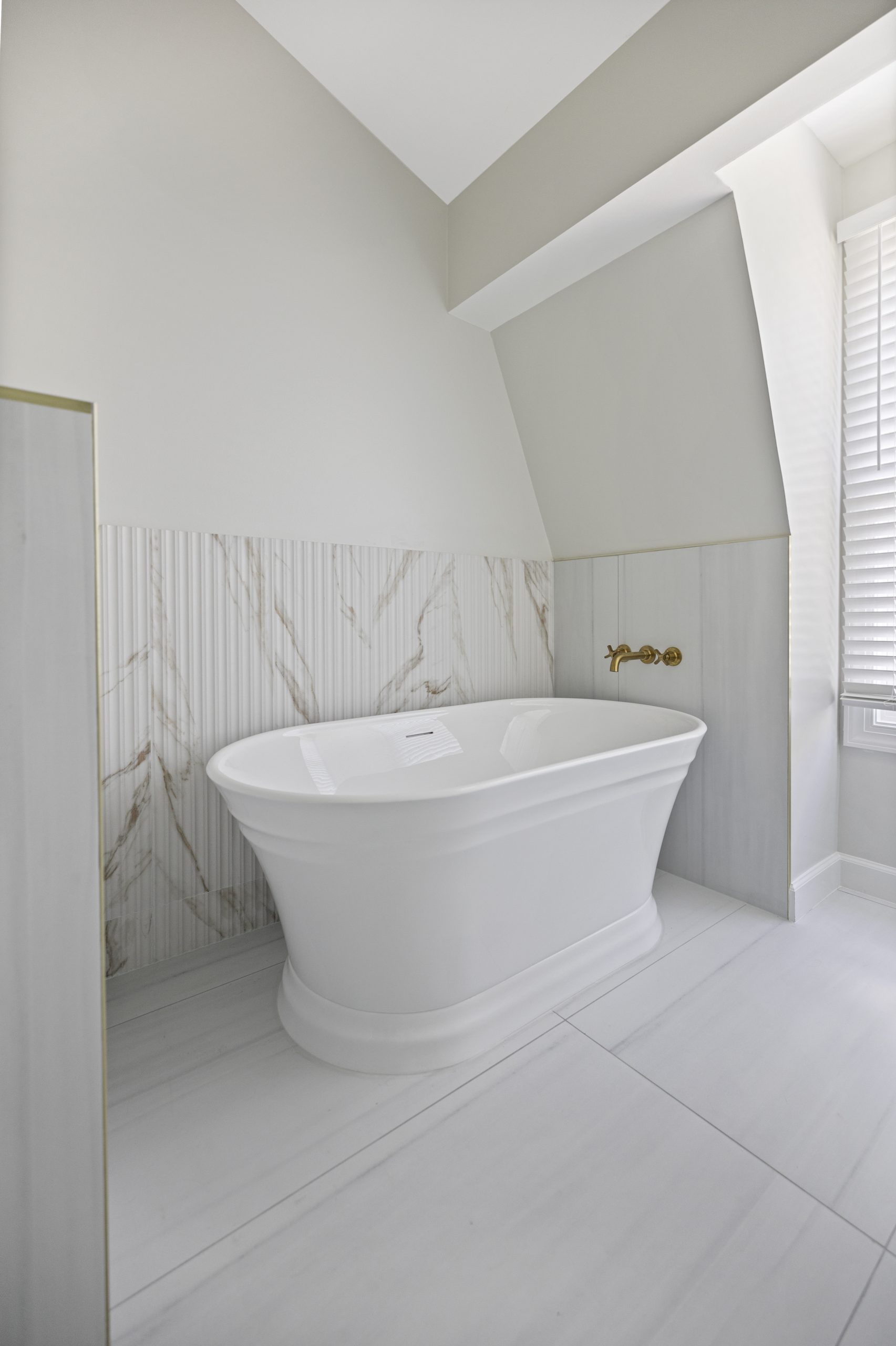 Freestanding tub with gold wall mounted faucet mixing warm metal against marble pattern tile