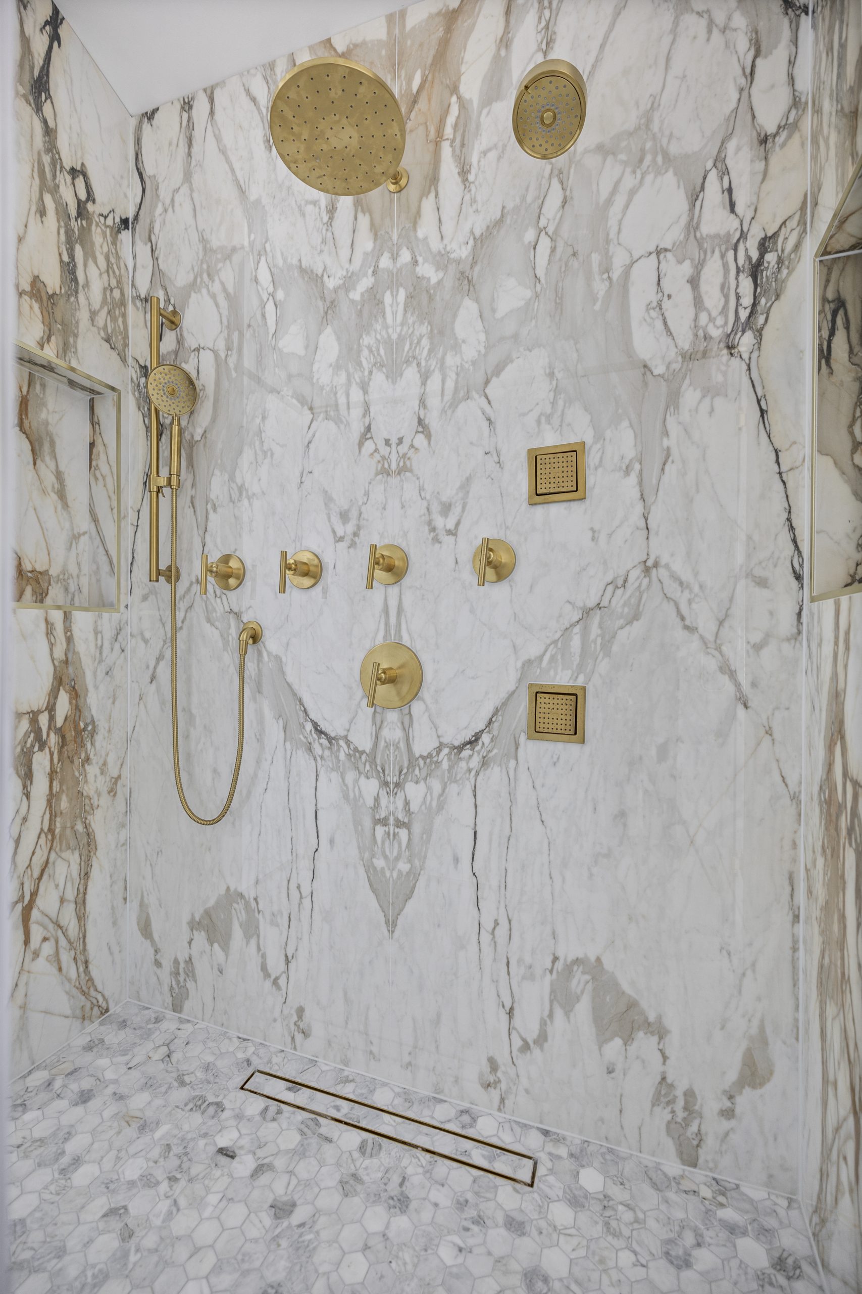 Marble shower with gold rain head and handheld fixtures mixed against cool stone tones