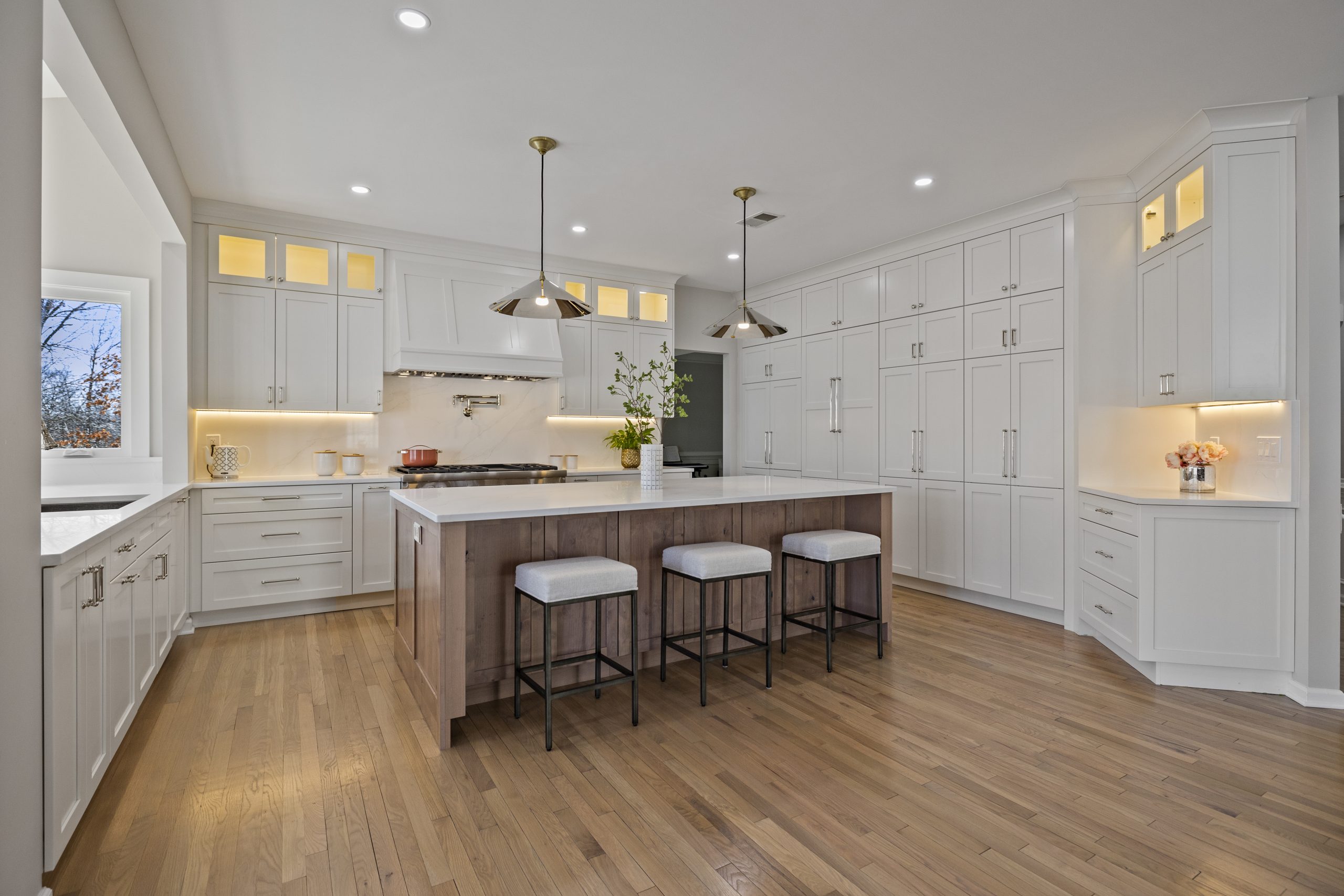 White kitchen with a wood island, three stools, pendant lights and pale wide plank hardwood floors