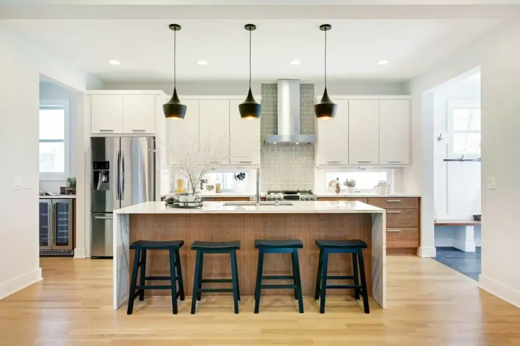 Modern kitchen features white cabinets, stainless steel appliances, island with four stools, and pendant lights.