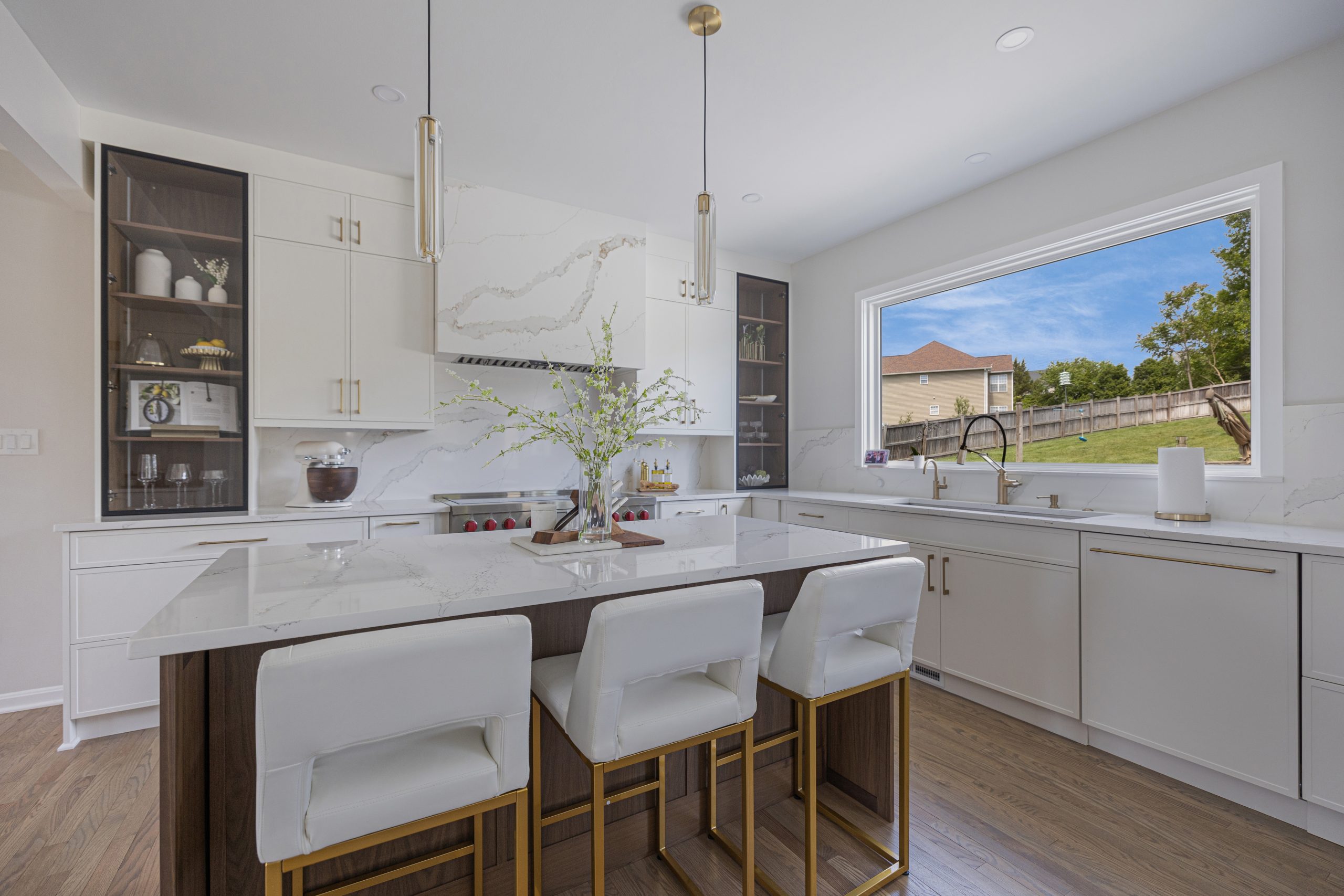 Custom kitchen island in Northern Virginia with marble look quartz top, walnut base, three upholstered stools and brass pendant lights
