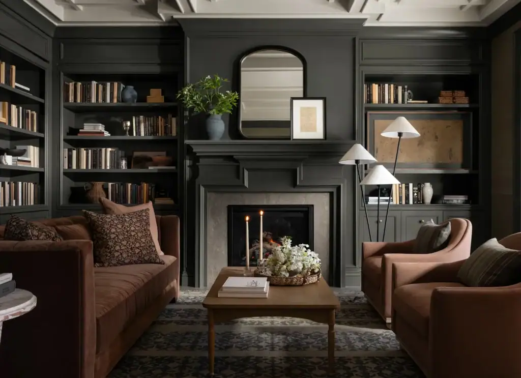 Cozy living room with dark walls, fireplace, bookshelves, brown sofas, coffee table, and floor lamps.