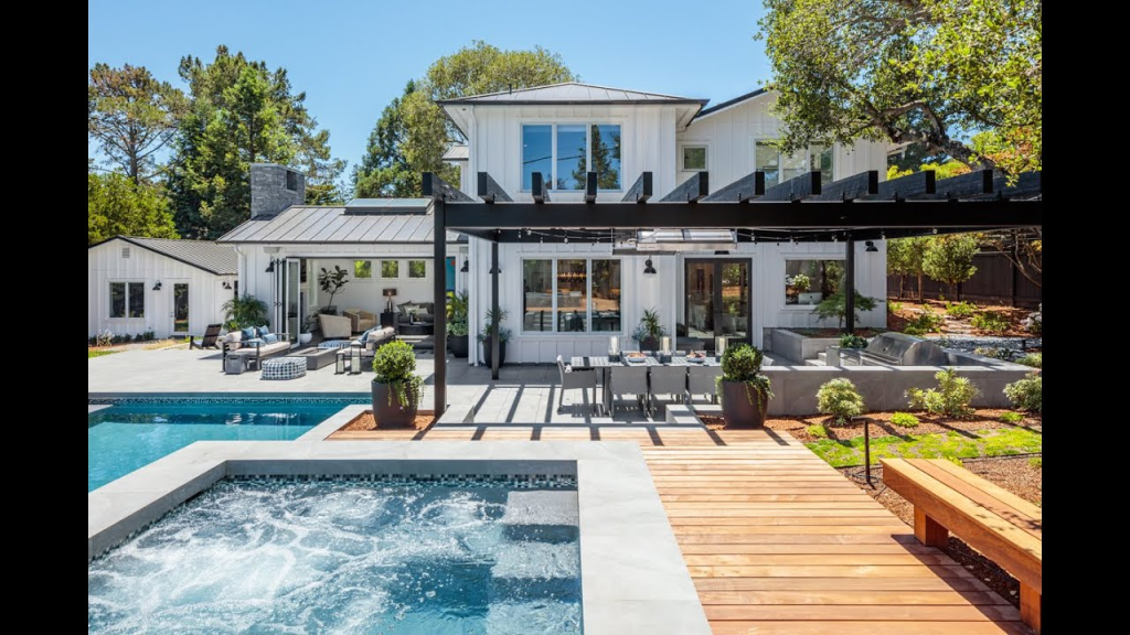 Modern house with large windows, a pergola, patio dining area, pool, and hot tub in a landscaped backyard.