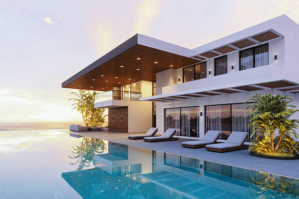 Modern luxury house features large windows, poolside lounge chairs, and palm trees mirrored in the pool.