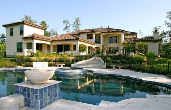 A large modern house features a terracotta roof, many windows, and a swimming pool in the foreground.