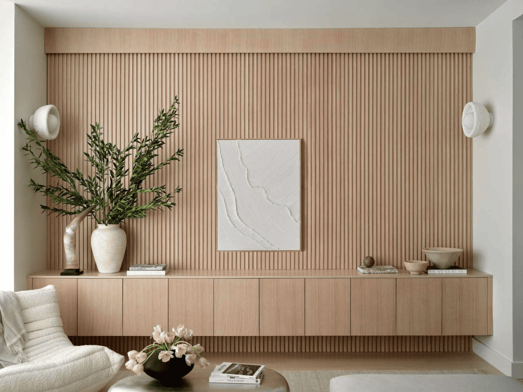 Minimalist living room with ribbed wood accent wall, floating console, art, and vases with greenery.
