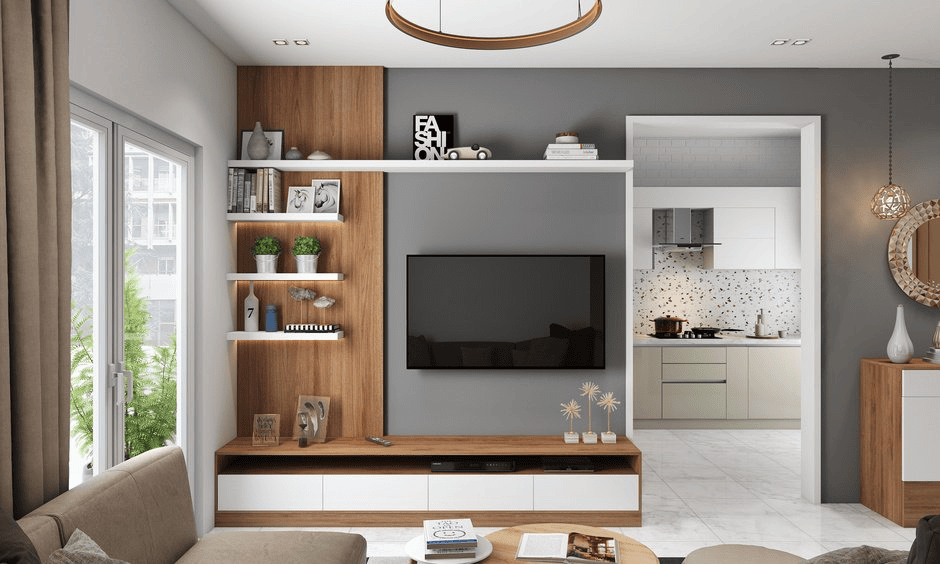 Modern living room with wall-mounted TV, shelves, lush plants, and open view into a bright white kitchen.
