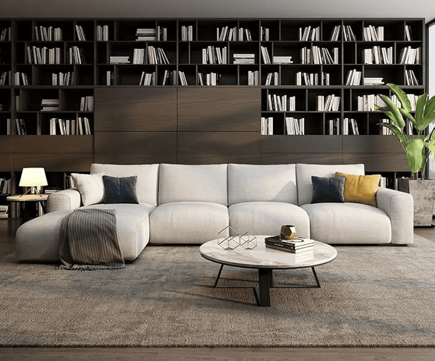 A modern living room features a large gray sectional sofa, round coffee table, and tall bookshelves behind.