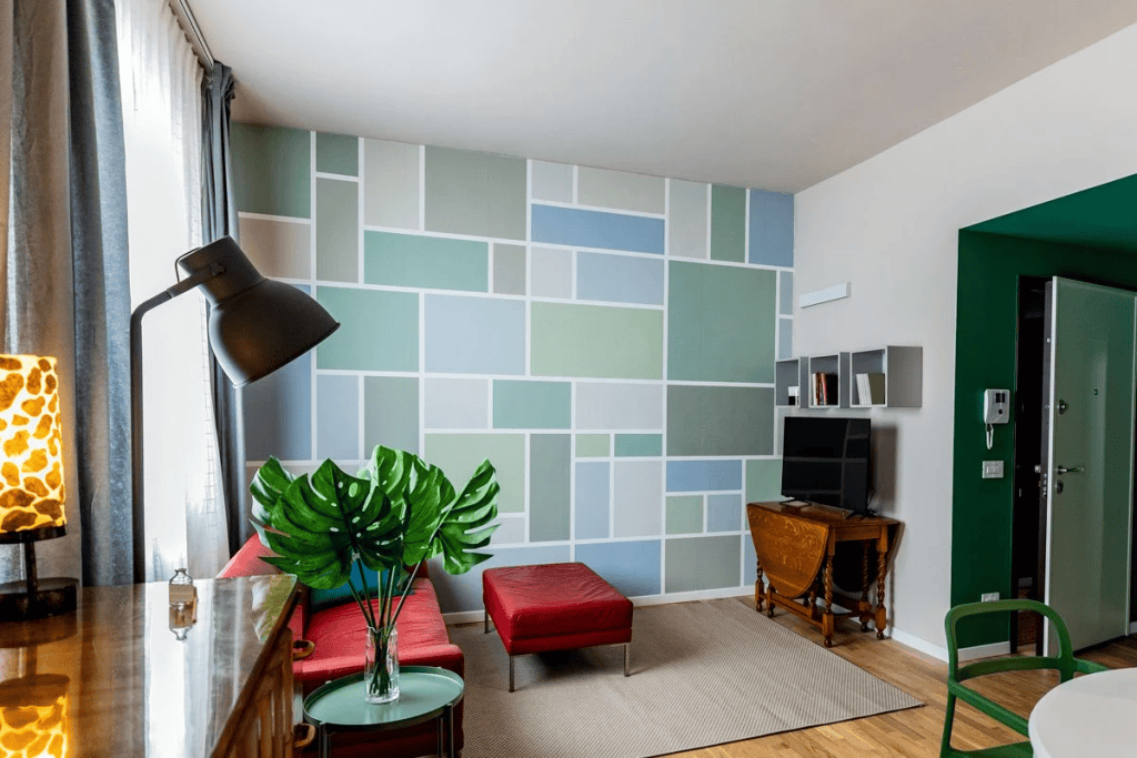 Colorful living room features geometric wall pattern, red sofa, green plants, and TV on wooden cabinet.