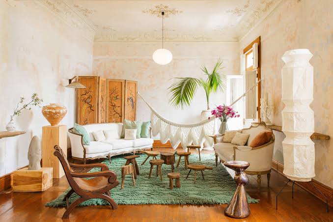 Bohemian living room featuring a green rug, hammock, eclectic furniture, lush plants, and ample natural light.