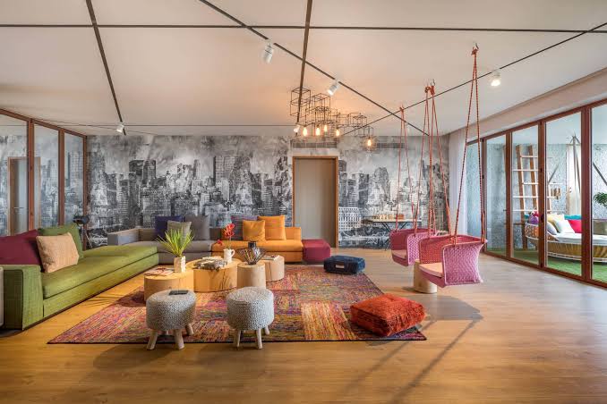 Colorful modern living room features a mural wall, swings, vibrant furniture, and large windows.