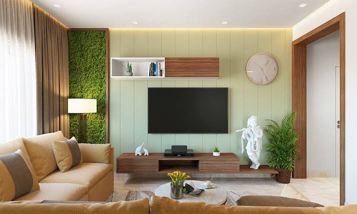 Modern living room with a wall-mounted TV, sofa, plants, and natural light streaming through windows.