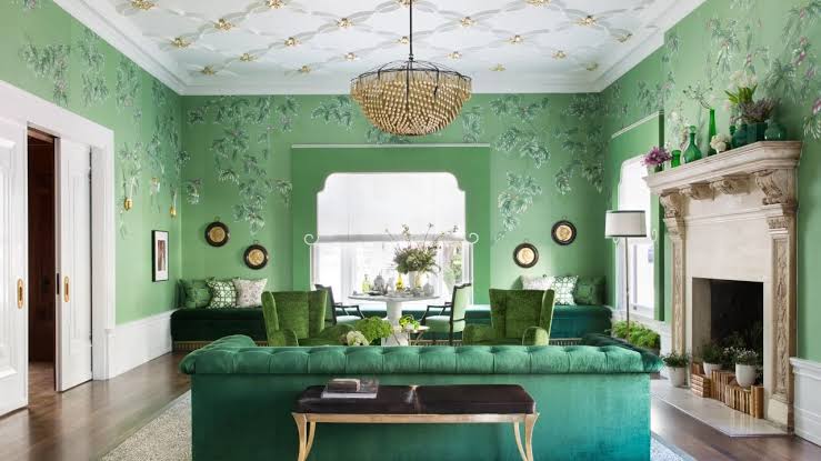 Elegant green living room with patterned wallpaper, velvet sofa, chandelier, and ornate fireplace mantel.