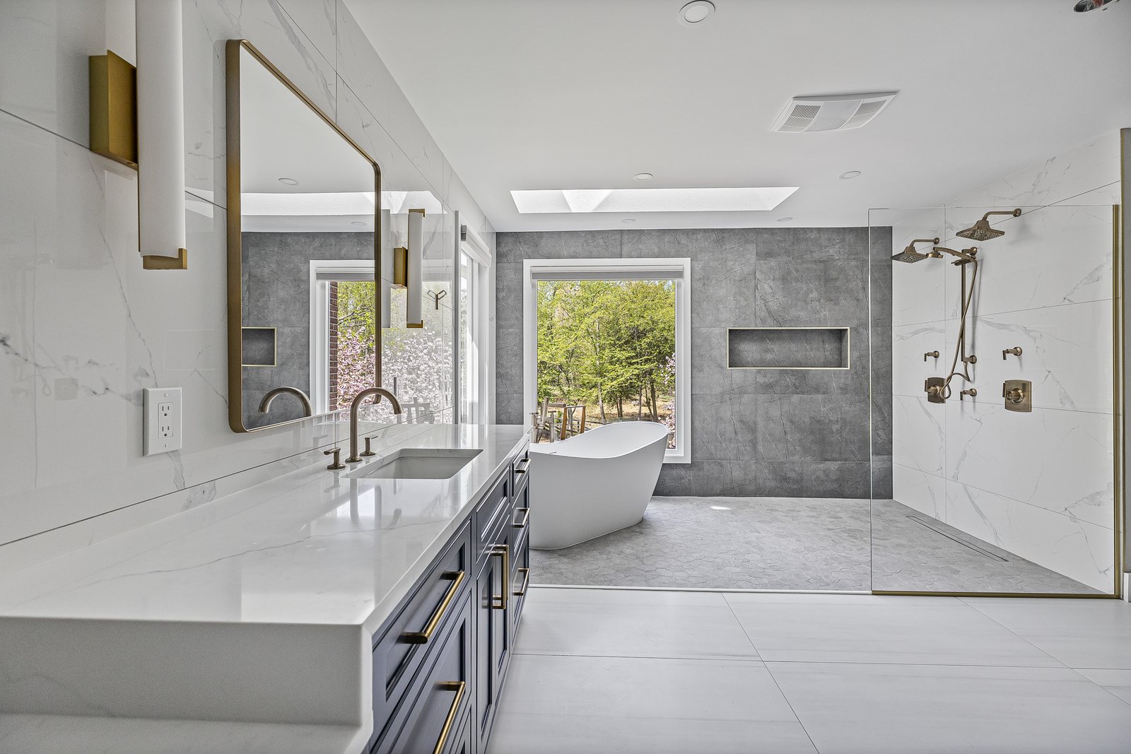 Gray and white primary bathroom with a skylight over a freestanding tub, a marble shower and brass fixtures