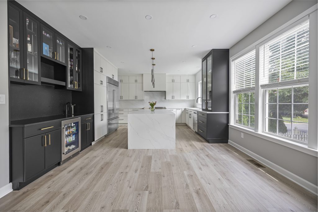 Modern kitchen featuring black and white cabinets, marble island, wood floors, and windows with blinds.