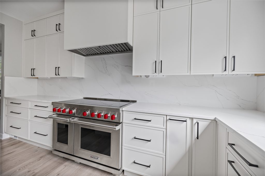 Modern kitchen featuring white cabinets, a marble backsplash, and a stainless steel stove with red knobs.