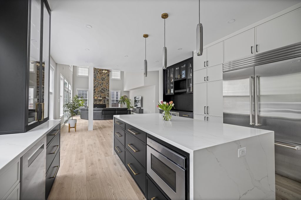 Remodeled Fairfax County kitchen with white cabinets, a black island, marble counters, pendant lights, and stainless appliances after final inspection.