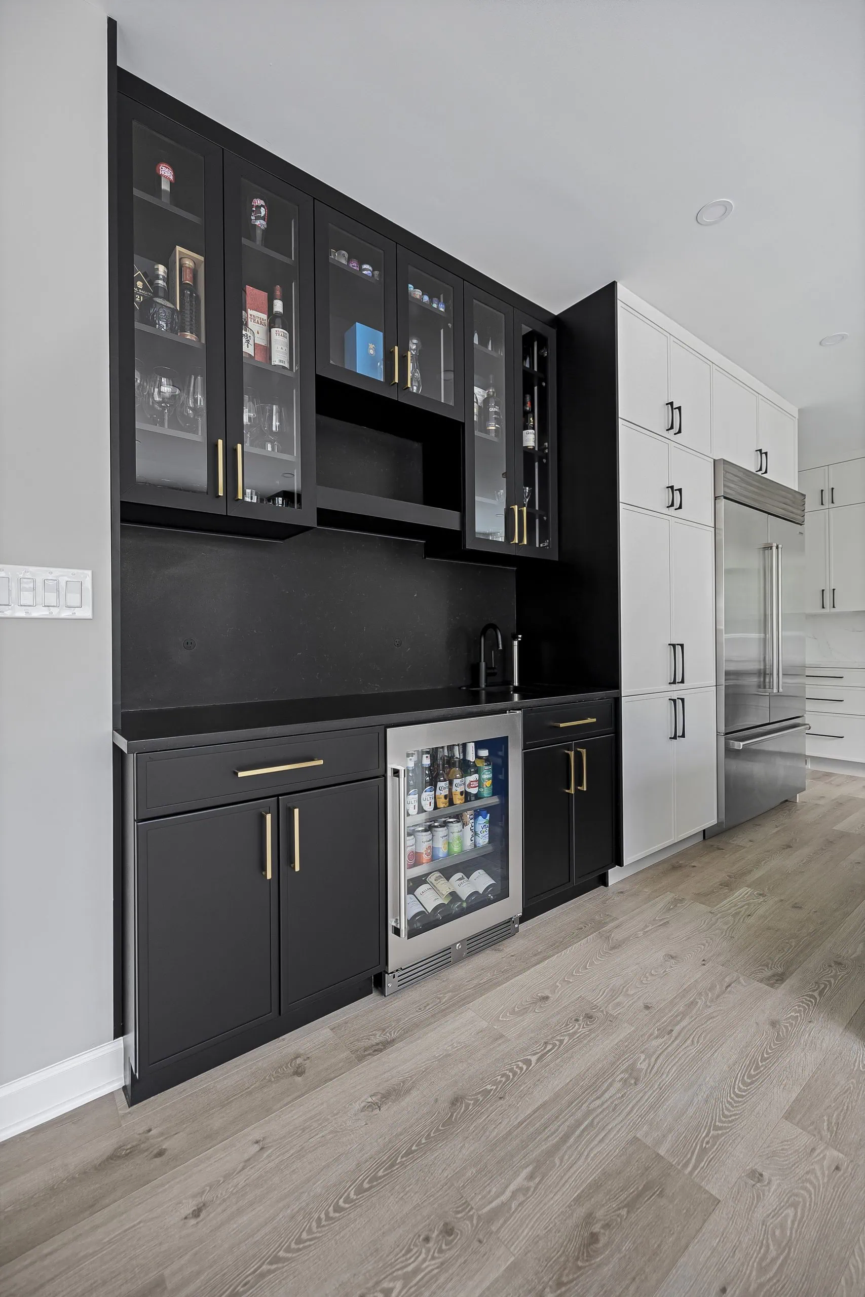 Black bar cabinets with gold hardware and stainless beverage fridge showing mixed metals in one design