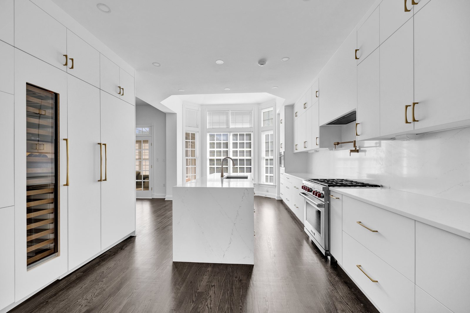 Kitchen with a walnut island, a calacatta marble range hood and backsplash, white cabinets and brass accents