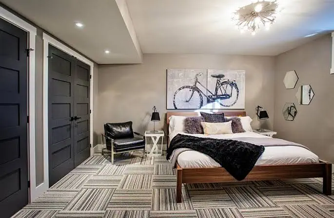 Modern bedroom with patterned carpet, black doors, bike wall art, chair, and a unique ceiling light.