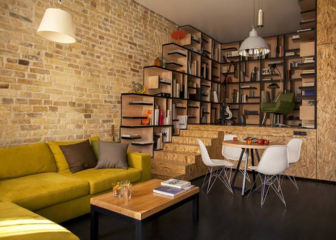Cozy living room with a yellow sofa, modern shelves, books, round dining table, and white chairs.