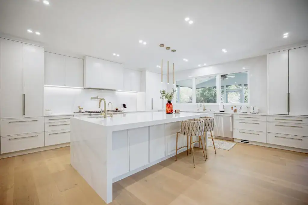 White kitchen with a large island, gold chairs and wood flooring in a remodeled Northern Virginia home