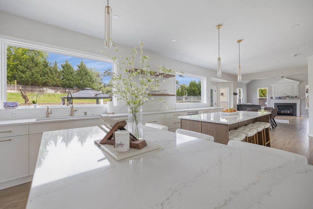 A spacious modern kitchen features a large marble island, white cabinetry, and backyard views.